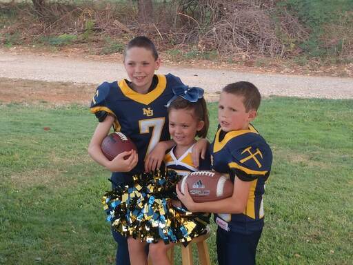 Two young boys on the Jr. football team wearing a blue and gold jersey, one young girl on the Jr. cheer leading team for football.